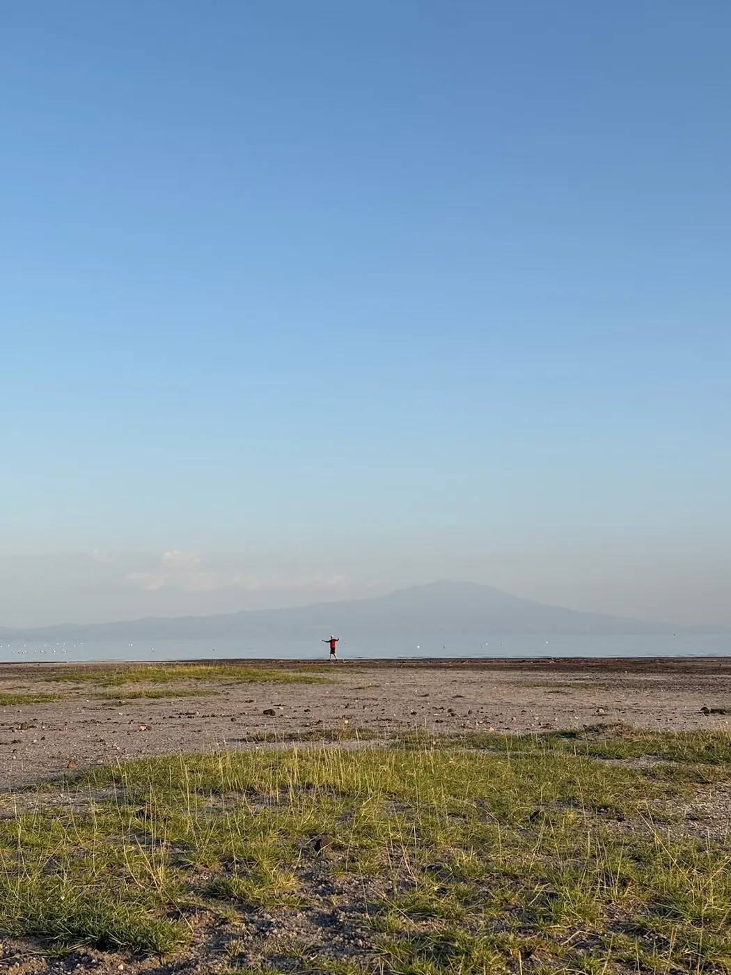 A bare shoreline flat and shallow lake below a hazy mountain